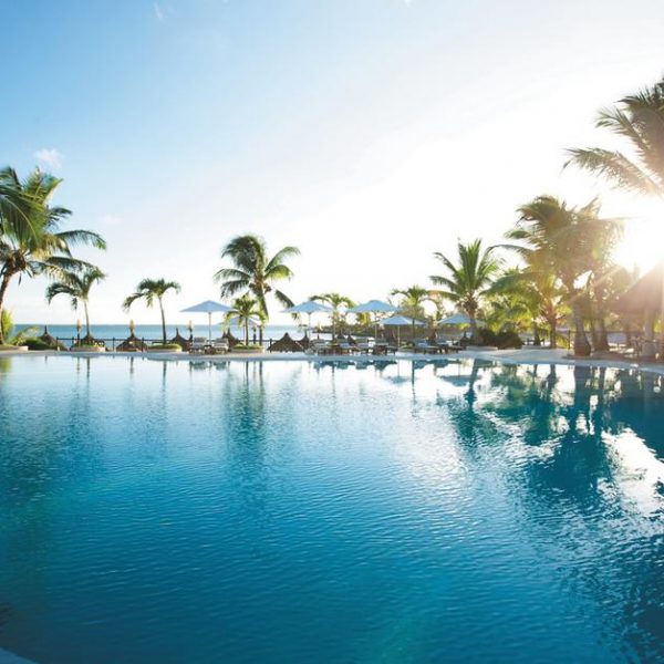 View of the swimming pool with the sun setting amongst the palm trees at LUX Grand Gaube in Mauritius
