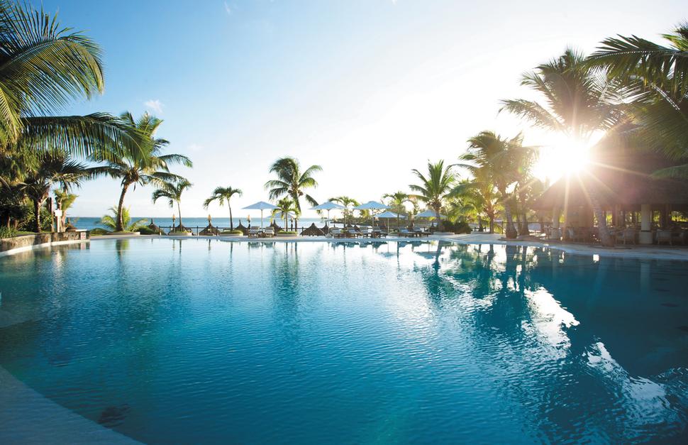View of the swimming pool with the sun setting amongst the palm trees at LUX Grand Gaube in Mauritius