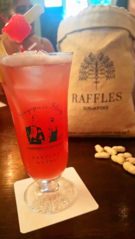 Close up of a Raffles Singapore Sling with a bag of peanuts in the background at Raffles Singapore Hotel